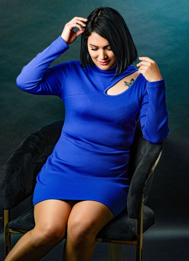 Een vrouw in een blauwe jurk zit op een stoel en raakt haar haar aan.