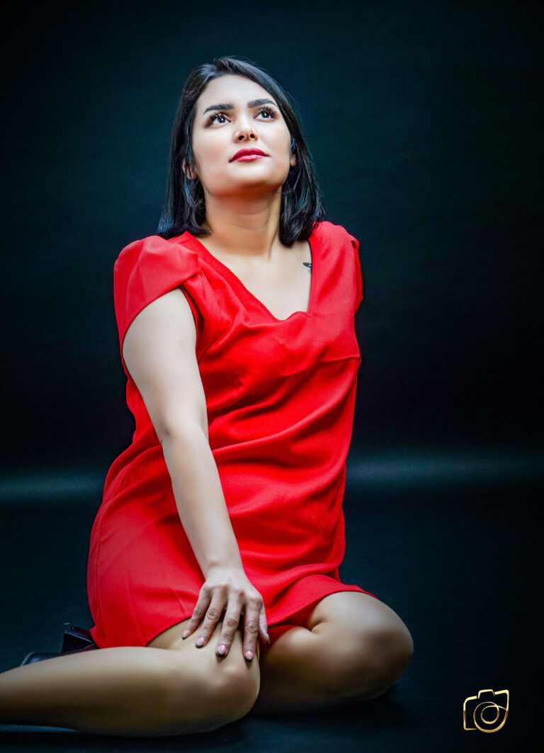 Een vrouw gekleed in een rode jurk zit op de grond en kijkt omhoog.