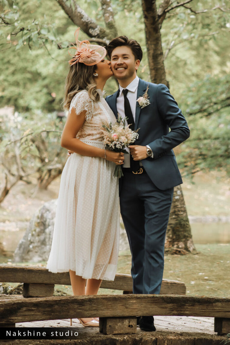Een gelukkig paar in trouwkleding omarmt elkaar liefdevol op een houten brug in een schilderachtig park.